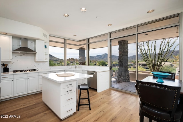 kitchen with appliances with stainless steel finishes, a kitchen island, white cabinets, a mountain view, and wall chimney exhaust hood