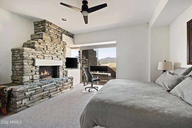 carpeted bedroom featuring a stone fireplace and ceiling fan