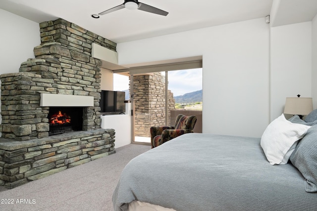 carpeted bedroom with ceiling fan, a stone fireplace, and access to exterior