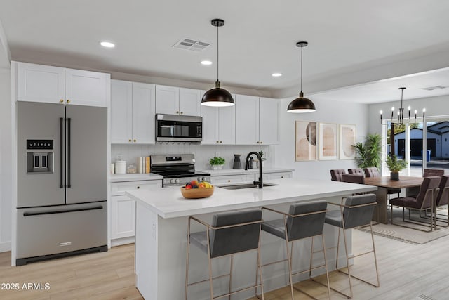 kitchen with a kitchen island with sink, sink, hanging light fixtures, and appliances with stainless steel finishes