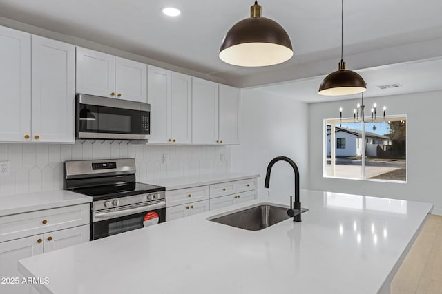 kitchen with tasteful backsplash, stainless steel appliances, sink, decorative light fixtures, and white cabinetry