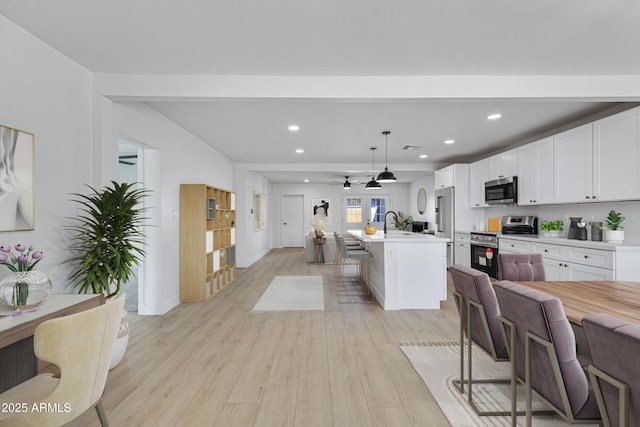 kitchen with hanging light fixtures, stainless steel appliances, a kitchen breakfast bar, a kitchen island with sink, and white cabinets