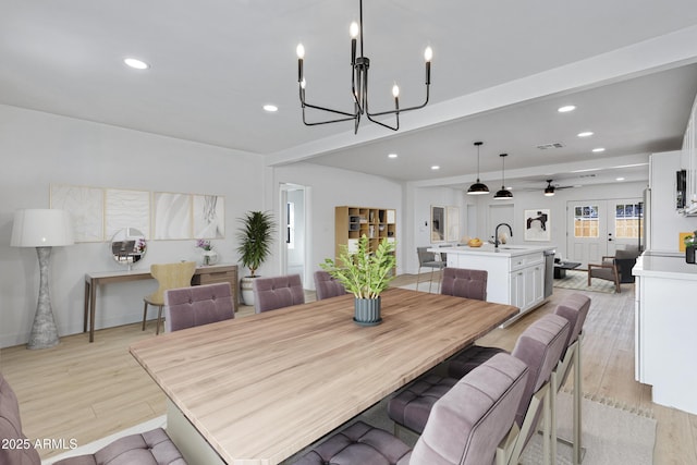 dining area with ceiling fan with notable chandelier, light wood-type flooring, beamed ceiling, and sink