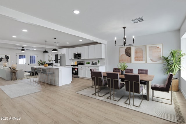 dining area featuring ceiling fan with notable chandelier, light wood-type flooring, sink, and french doors