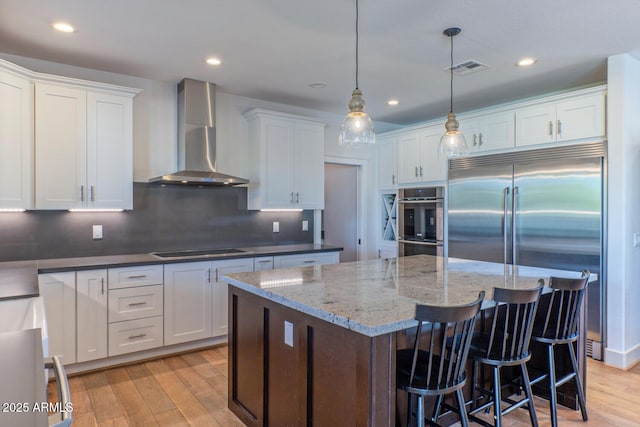 kitchen with stainless steel appliances, white cabinetry, wall chimney exhaust hood, and decorative light fixtures