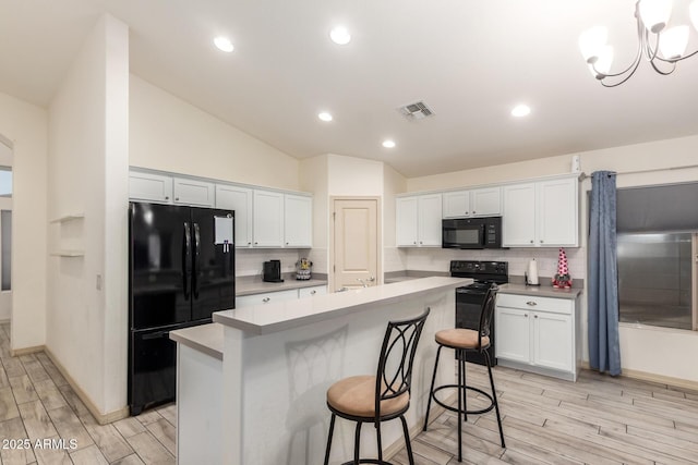 kitchen with a center island with sink, white cabinets, a kitchen breakfast bar, and black appliances