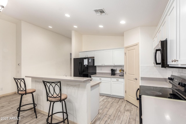 kitchen with a kitchen breakfast bar, a center island, black appliances, white cabinets, and vaulted ceiling