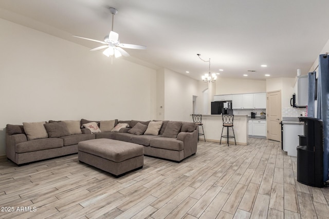 living room with vaulted ceiling, ceiling fan with notable chandelier, and light hardwood / wood-style floors