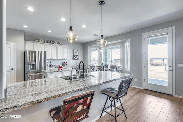 kitchen with white cabinets, a center island with sink, hanging light fixtures, stainless steel fridge with ice dispenser, and a breakfast bar area