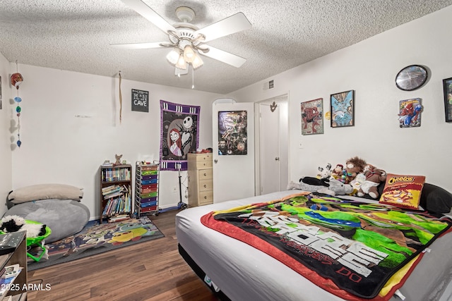 bedroom featuring a ceiling fan, a textured ceiling, visible vents, and wood finished floors