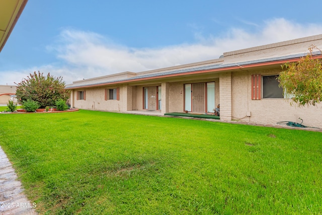 rear view of property featuring stucco siding, brick siding, and a yard