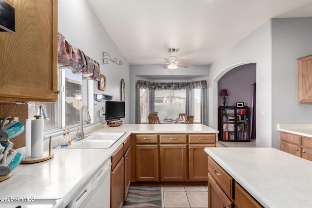 kitchen featuring brown cabinets, light countertops, a sink, dishwasher, and a peninsula