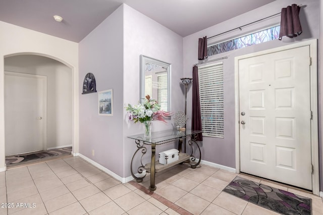 entrance foyer featuring arched walkways, a healthy amount of sunlight, baseboards, and light tile patterned floors