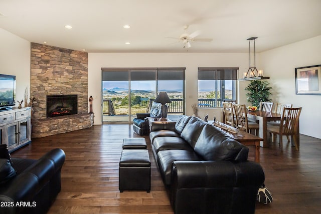 living room featuring dark hardwood / wood-style floors, ceiling fan, a stone fireplace, and a mountain view