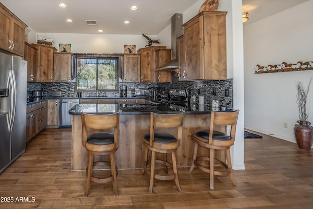 kitchen featuring dark hardwood / wood-style flooring, appliances with stainless steel finishes, a kitchen breakfast bar, and wall chimney exhaust hood