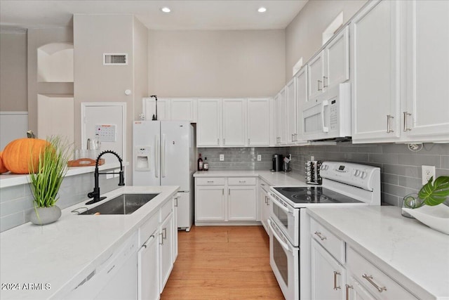 kitchen featuring white appliances, sink, light wood-type flooring, backsplash, and white cabinets