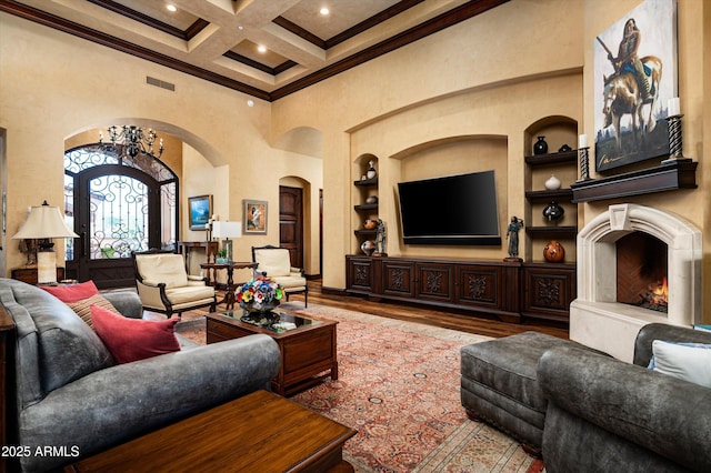 living area featuring a towering ceiling, arched walkways, wood finished floors, built in features, and beamed ceiling