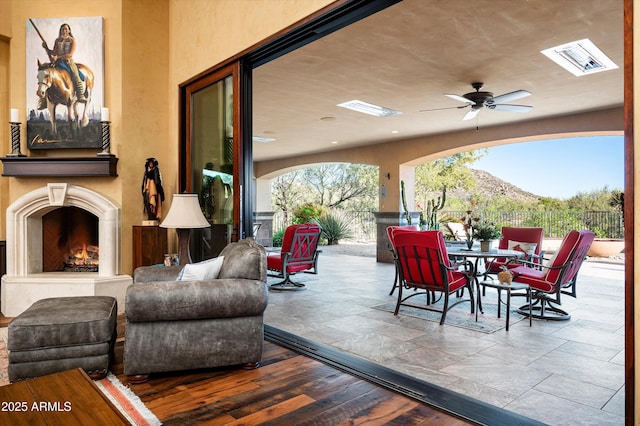 view of patio featuring fence, a warm lit fireplace, outdoor dining area, and ceiling fan
