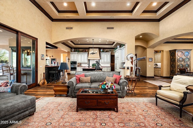 living area featuring arched walkways, crown molding, a towering ceiling, wood-type flooring, and baseboards