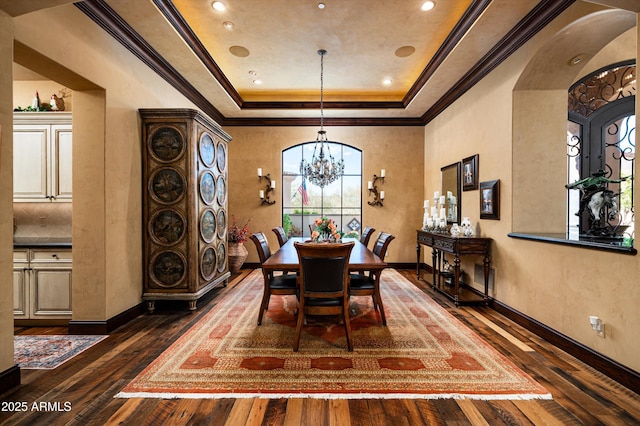 dining room with a tray ceiling, dark wood-style floors, a chandelier, baseboards, and crown molding