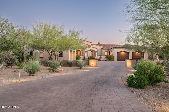 mediterranean / spanish-style home featuring curved driveway, stucco siding, a garage, and a tiled roof