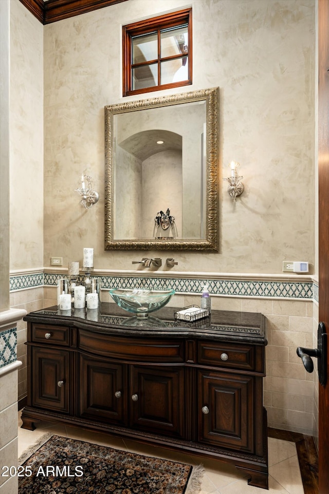 half bathroom featuring tile walls, tile patterned flooring, vanity, a wainscoted wall, and crown molding
