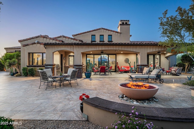 rear view of property with a patio, ceiling fan, a chimney, an outdoor fire pit, and a tile roof