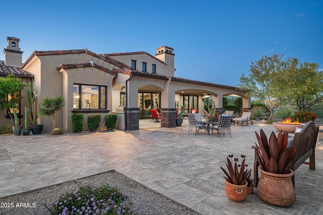 rear view of house with a fire pit, a chimney, a patio, a tiled roof, and stucco siding