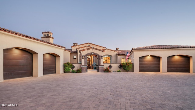 mediterranean / spanish-style house featuring stucco siding, a garage, a chimney, and a tile roof