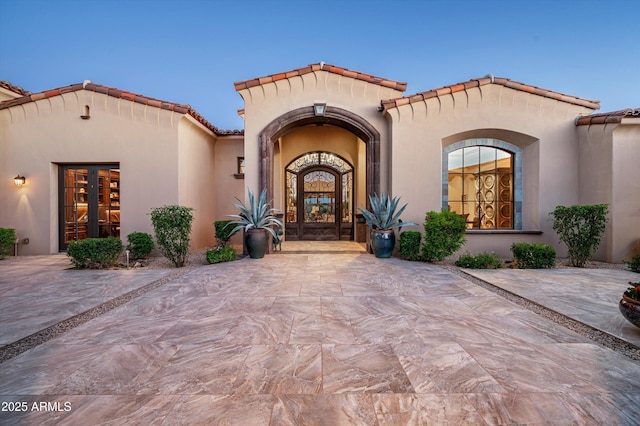 view of exterior entry with a tiled roof, stucco siding, and french doors