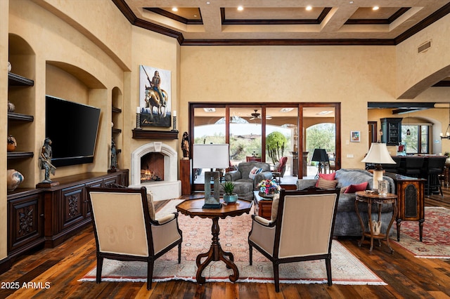 living room featuring a high ceiling, ornamental molding, a warm lit fireplace, dark wood-type flooring, and built in features