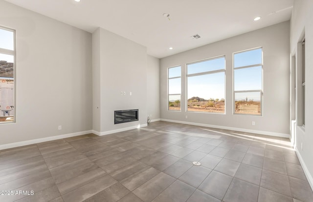 unfurnished living room with visible vents, baseboards, a glass covered fireplace, tile patterned flooring, and recessed lighting