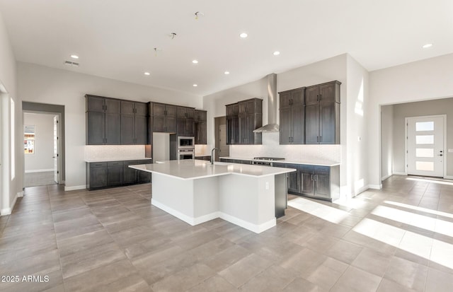 kitchen featuring an island with sink, wall chimney exhaust hood, light countertops, gas cooktop, and a sink