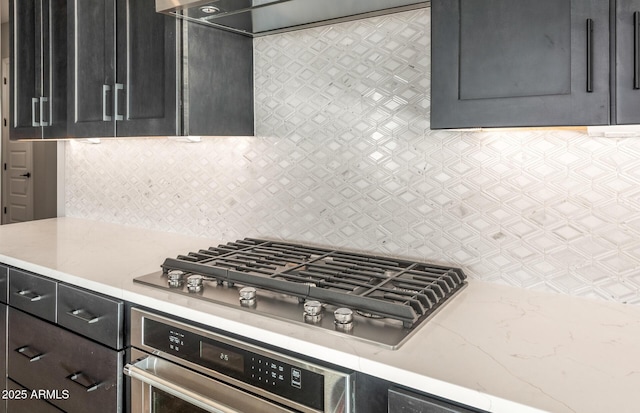 kitchen featuring wall chimney exhaust hood, appliances with stainless steel finishes, dark cabinetry, and tasteful backsplash