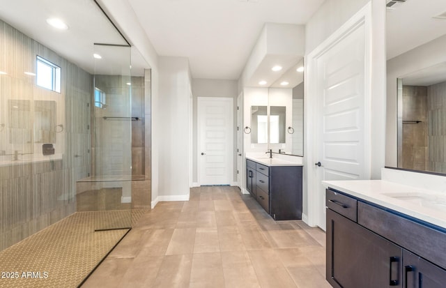 full bathroom with two vanities, baseboards, a walk in shower, and a sink