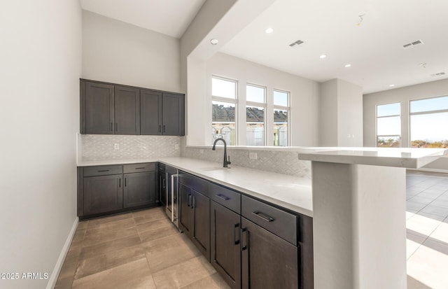 kitchen with tasteful backsplash, baseboards, visible vents, a peninsula, and a sink