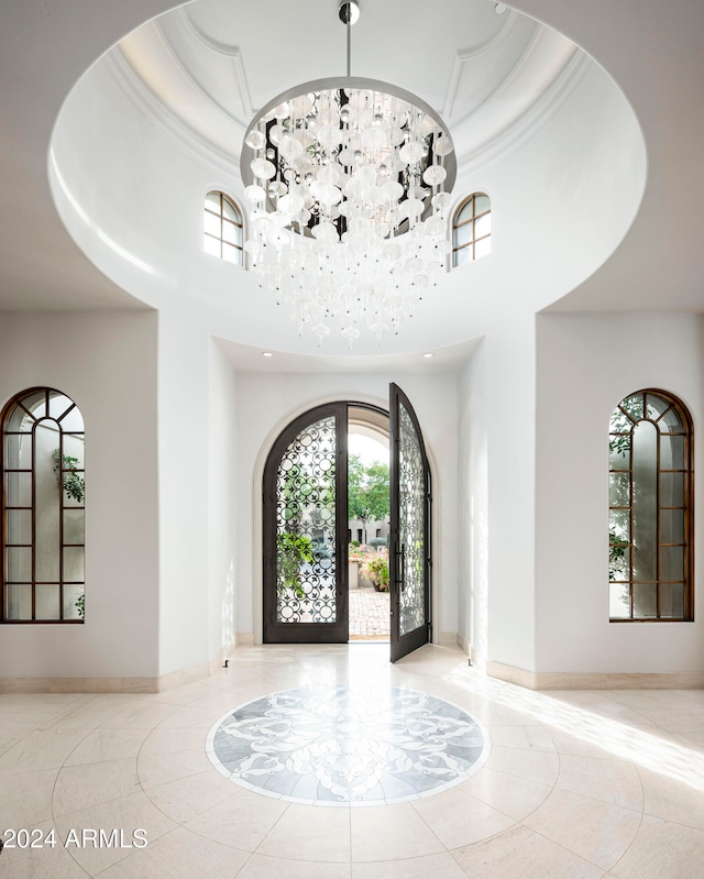 tiled foyer with a chandelier, a towering ceiling, a tray ceiling, and french doors