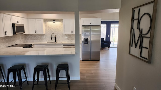 kitchen featuring appliances with stainless steel finishes, white cabinetry, sink, a kitchen bar, and kitchen peninsula