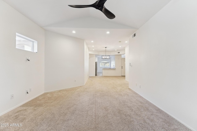 unfurnished living room with vaulted ceiling, light colored carpet, a wealth of natural light, and ceiling fan with notable chandelier