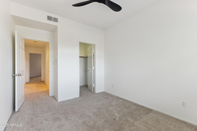 unfurnished bedroom with light carpet, a walk in closet, ceiling fan, and a closet