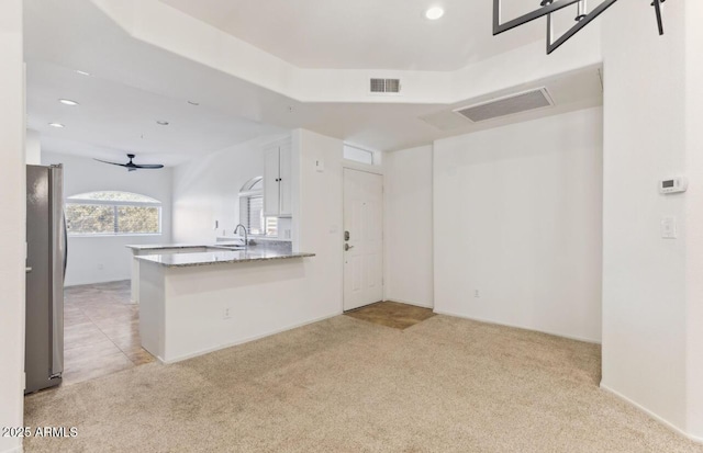 kitchen with light carpet, kitchen peninsula, stainless steel fridge, white cabinets, and sink