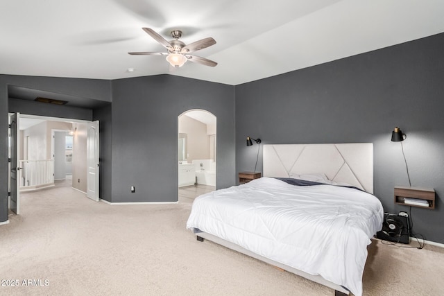 carpeted bedroom with arched walkways, lofted ceiling, a ceiling fan, baseboards, and ensuite bath