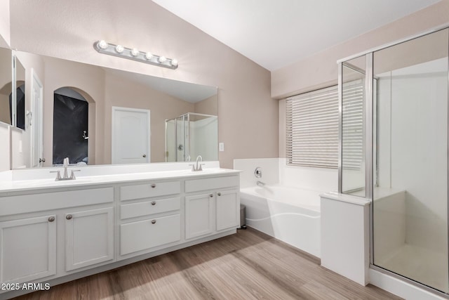 full bathroom with a garden tub, double vanity, a sink, a shower stall, and wood finished floors