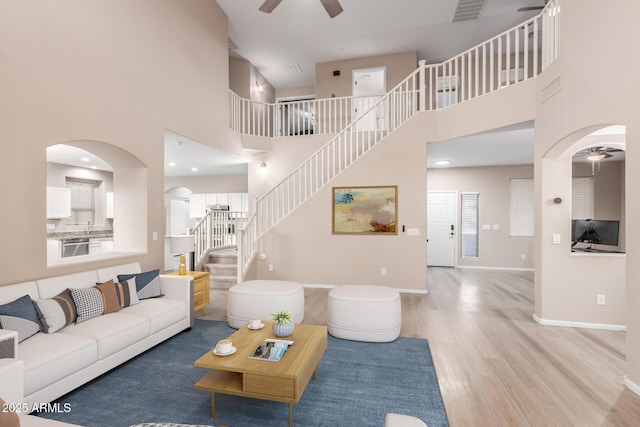 living room featuring baseboards, visible vents, a ceiling fan, wood finished floors, and stairs