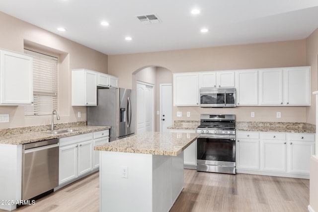 kitchen with arched walkways, stainless steel appliances, a sink, visible vents, and light wood-style floors