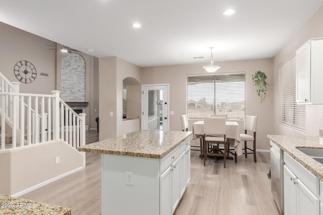 kitchen featuring arched walkways, a center island, light wood finished floors, white cabinetry, and ceiling fan