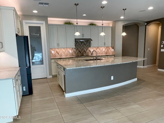 kitchen with sink, black fridge, pendant lighting, decorative backsplash, and a center island with sink