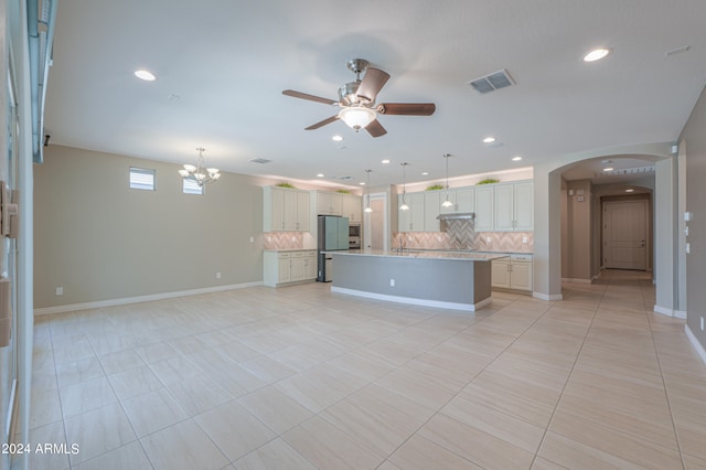 kitchen featuring tasteful backsplash, a center island with sink, white cabinets, and decorative light fixtures