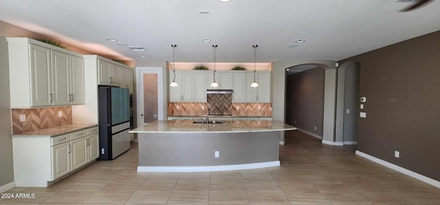 kitchen featuring backsplash, light stone counters, light tile patterned floors, decorative light fixtures, and a center island with sink