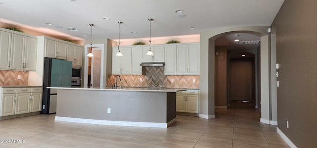 kitchen with decorative backsplash, hanging light fixtures, an island with sink, fridge, and light tile patterned flooring